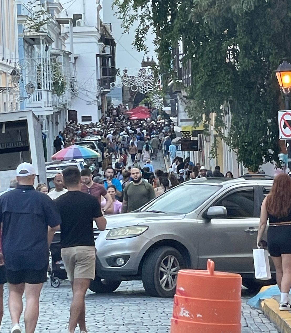 Multitud de peatones llenando la Calle del Cristo esquina Fortaleza mientras un carro intenta cruzar entre la gente
